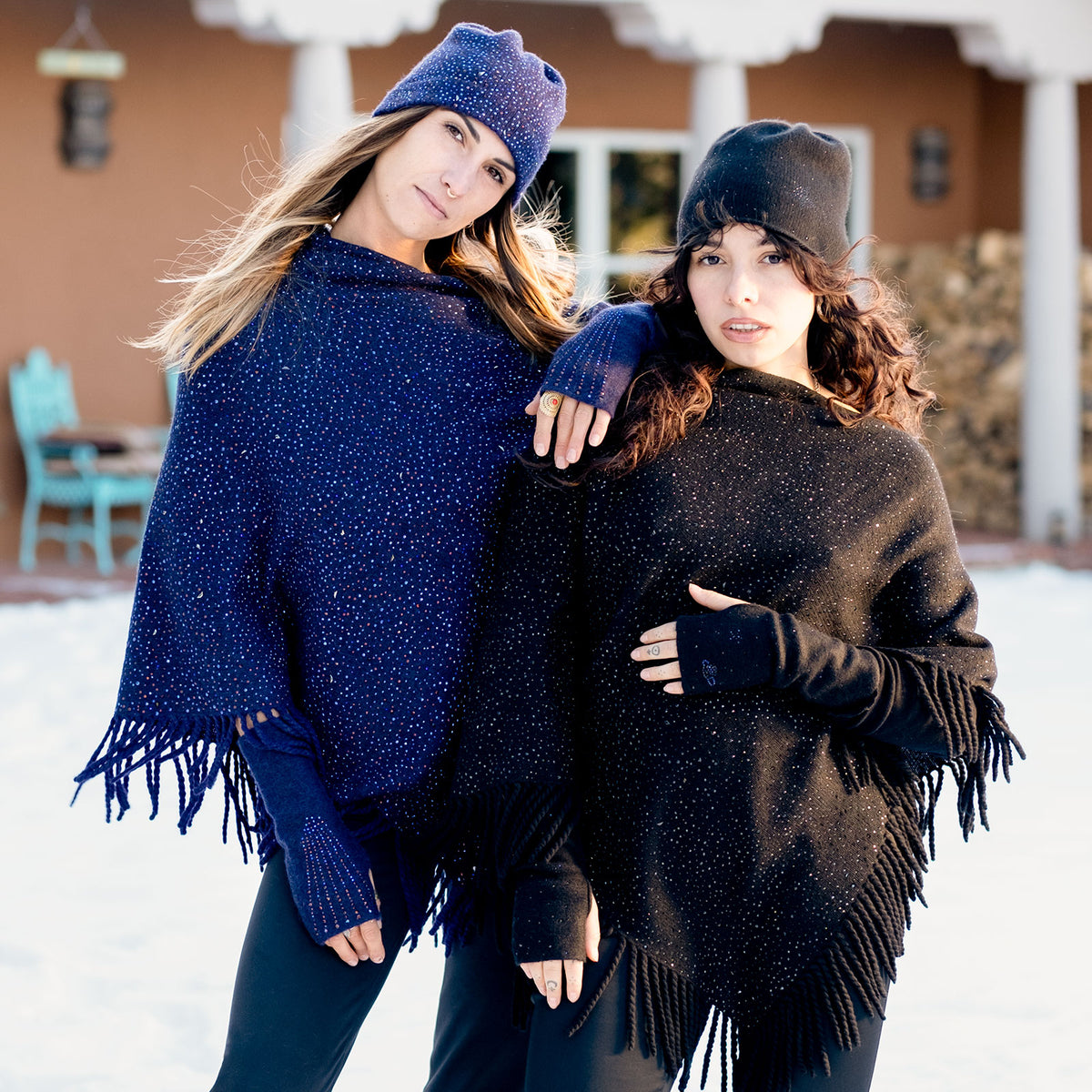 Two women standing in a snowy courtyard wearing luxury cashmere ponchos with fringe and thousands of Swarovski crystals. editorial-image