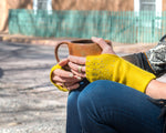 Pair of hands holding a coffee cup showcasing a pair of Turmeric colored Lattice Fingerless Gloves embellished with tiny luxury crystals and metal rhinestuds. editorial-image