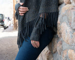 Assam colored Static Fringe Fingerless Gloves worn by a woman leaning against a rock wall. editorial-image